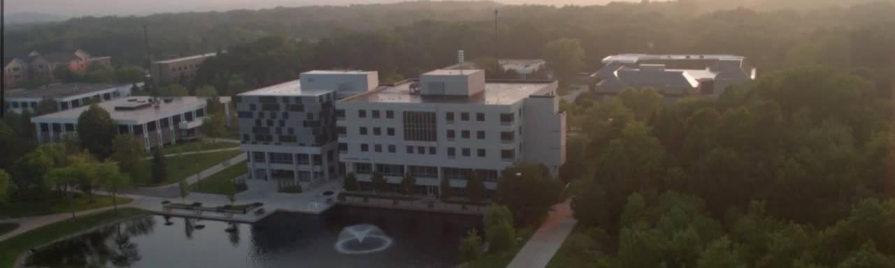 Aerial shot of a grey and blue square building near a small pond. GVSU 艾伦代尔校区的尊伯格大厅